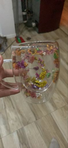 a person holding a wine glass with flowers in it on the floor next to a cat