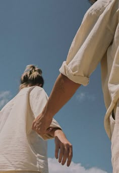 two people hold hands as they stand under a blue sky