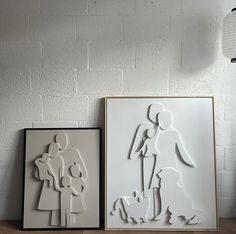 two paper cut art pieces sitting on top of a wooden table next to each other