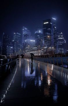 a person with an umbrella standing in the rain at night near a cityscape