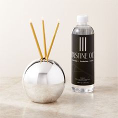 a bottle of perfume sitting next to a silver vase with sticks sticking out of it