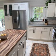 a kitchen with white cabinets and an area rug in front of the counter top that has a bowl of fruit on it