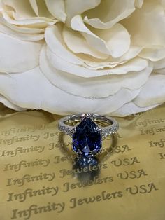 a blue diamond ring sitting on top of a piece of paper next to a white rose