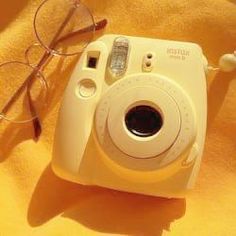 a white camera and some glasses on a yellow blanket with a black eyeglasses