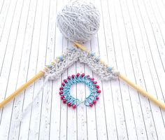 a ball of yarn sitting on top of a wooden floor next to two knitting needles