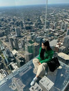 a woman sitting on top of a tall building looking down at the city from high up