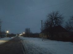 an empty street at night with snow on the ground and power lines in the distance