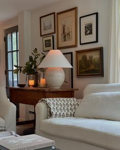 a living room filled with white furniture and pictures on the wall above it's windows