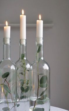 three glass bottles with plants in them sitting on a table next to two lit candles