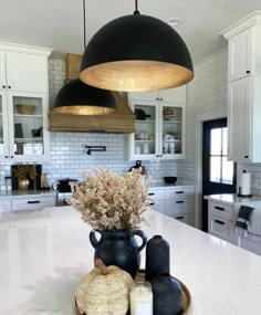 a large kitchen with white cabinets and black pendant lights over the countertop, along with two vases filled with dried flowers