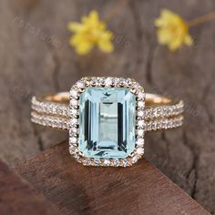 an aqua blue topazte and diamond ring on a piece of wood with flowers in the background