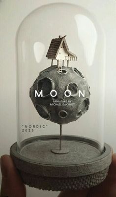 someone is holding up a glass dome with a house on it and the words moon underneath