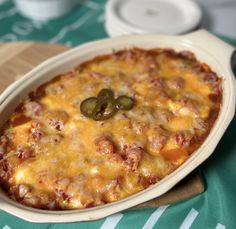 a casserole dish with cheese, meat and green olives in it on a table