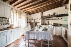 a dining table in a kitchen with white cupboards and wooden beams on the ceiling