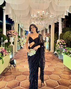 a woman in a black sari standing under a chandelier