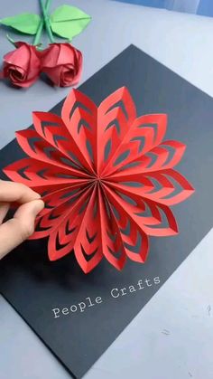 someone is making a paper flower out of red and black paper, with one hand