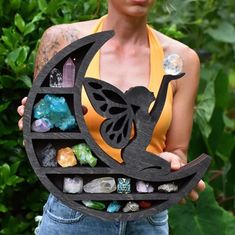 a woman holding up a wooden plaque with crystals and a butterfly on it's back