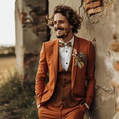 a man wearing an orange suit and bow tie leaning against a wall with his hands in his pockets