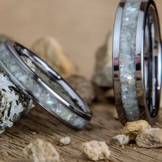 two wedding rings sitting next to each other on top of a wooden table covered in rocks