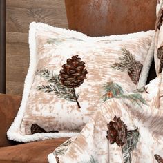 two pillows with pine cones on them are sitting on a chair next to a potted plant