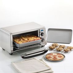 a toaster oven with pizzas and cookies in front of it on a table