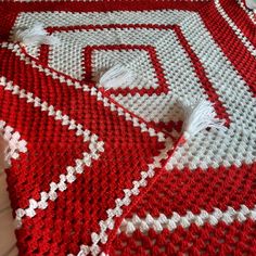 red and white crocheted afghan with tassels laying on top of it