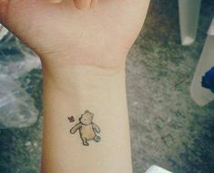 a small tattoo on the wrist of a girl with a teddy bear holding a flower