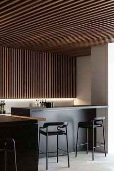 a modern kitchen with bar stools next to the counter and an overhead wooden slatted ceiling