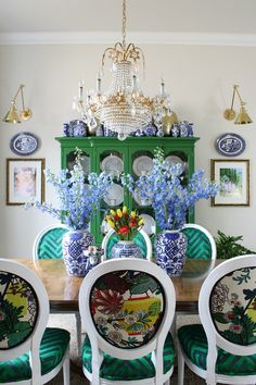 a dining room table with blue and white china cabinet in the corner, surrounded by green chairs