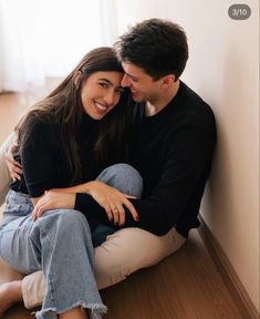 a man and woman sitting next to each other on top of a wooden floor in front of a window