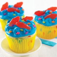 three cupcakes with blue frosting and sprinkles are on a plate