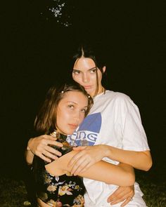 two young women hugging each other in the dark, one is wearing a t - shirt