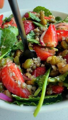 a salad with spinach, strawberries, and other vegetables in a white bowl