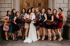 a group of women standing next to each other in front of a building holding bouquets