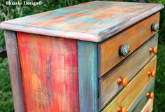 a multicolored wooden dresser sitting in the grass