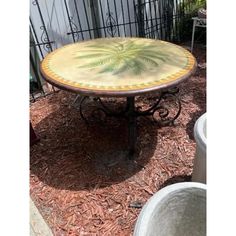 a round table with a palm tree painted on it's top sitting in front of a fence