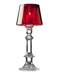 a red candle is lit on top of a clear glass table lamp with a red shade