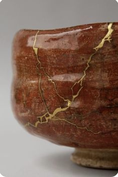 a close up of a red and gold vase on a white surface with a gray background