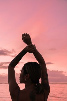 a woman standing on top of a beach next to the ocean holding her arms in the air