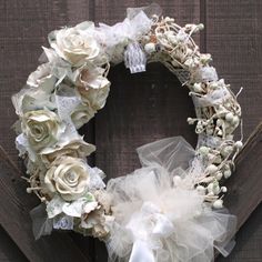 a wreath with white flowers and tulle is hanging on a wooden door, next to a bow