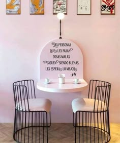 two chairs sitting at a table in front of a wall with pictures on the walls