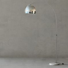 the floor lamp is next to a concrete wall with a white base and chrome shade