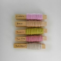 four skeins of yarn are lined up on wooden pegs and labeled with names