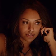 a beautiful young woman talking on a cell phone in a dark room with her hand to her ear