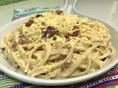 a white bowl filled with pasta and sauce on top of a colorful table cloth next to a fork