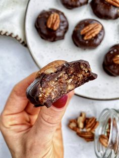 a hand holding a half eaten chocolate pecan cookie with walnuts in the background