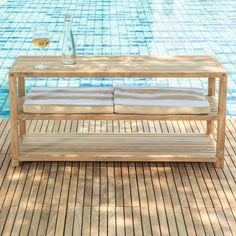 a wooden table sitting next to a swimming pool with two glasses of wine on it