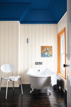 a white bath tub sitting in a bathroom next to a chair and painting on the wall