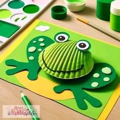 a paper frog craft is sitting on a table with paint and crayons around it