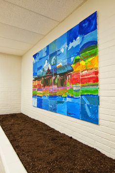 an empty room with white brick walls and colorful paintings on the wall above dirt in front of it